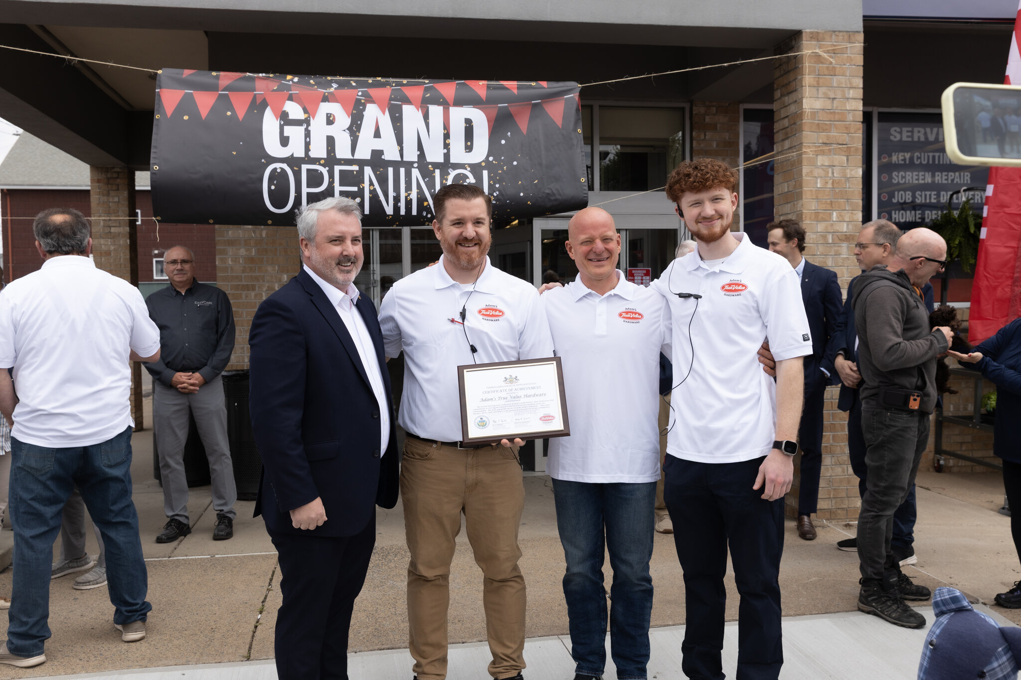 Chris and Justin Taffera with a True Value representative holding a Congratulations plaque on opening day