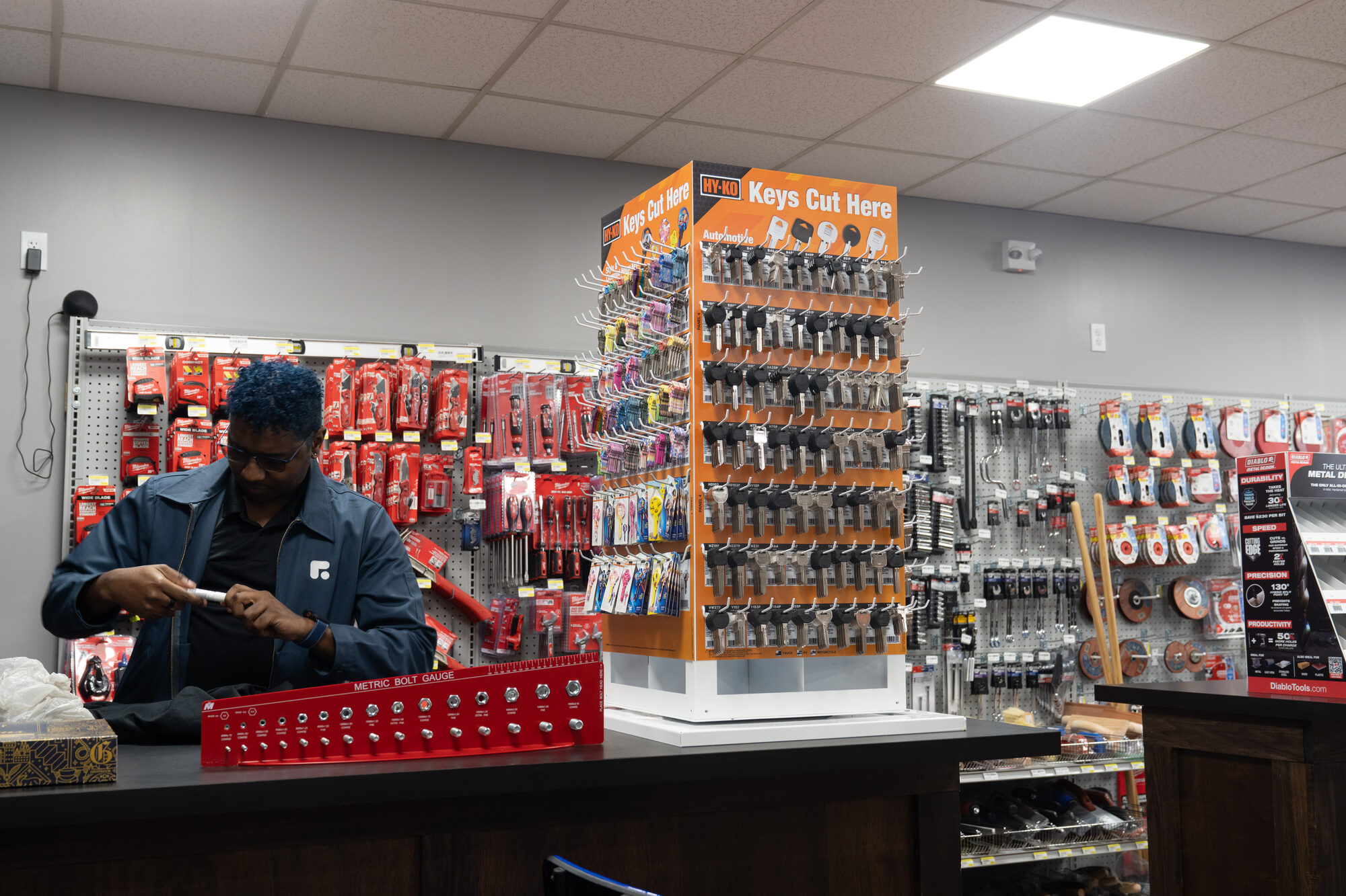 A Wigal Hardware employee cutting a key at the counter, next to the Keys Cut Here display